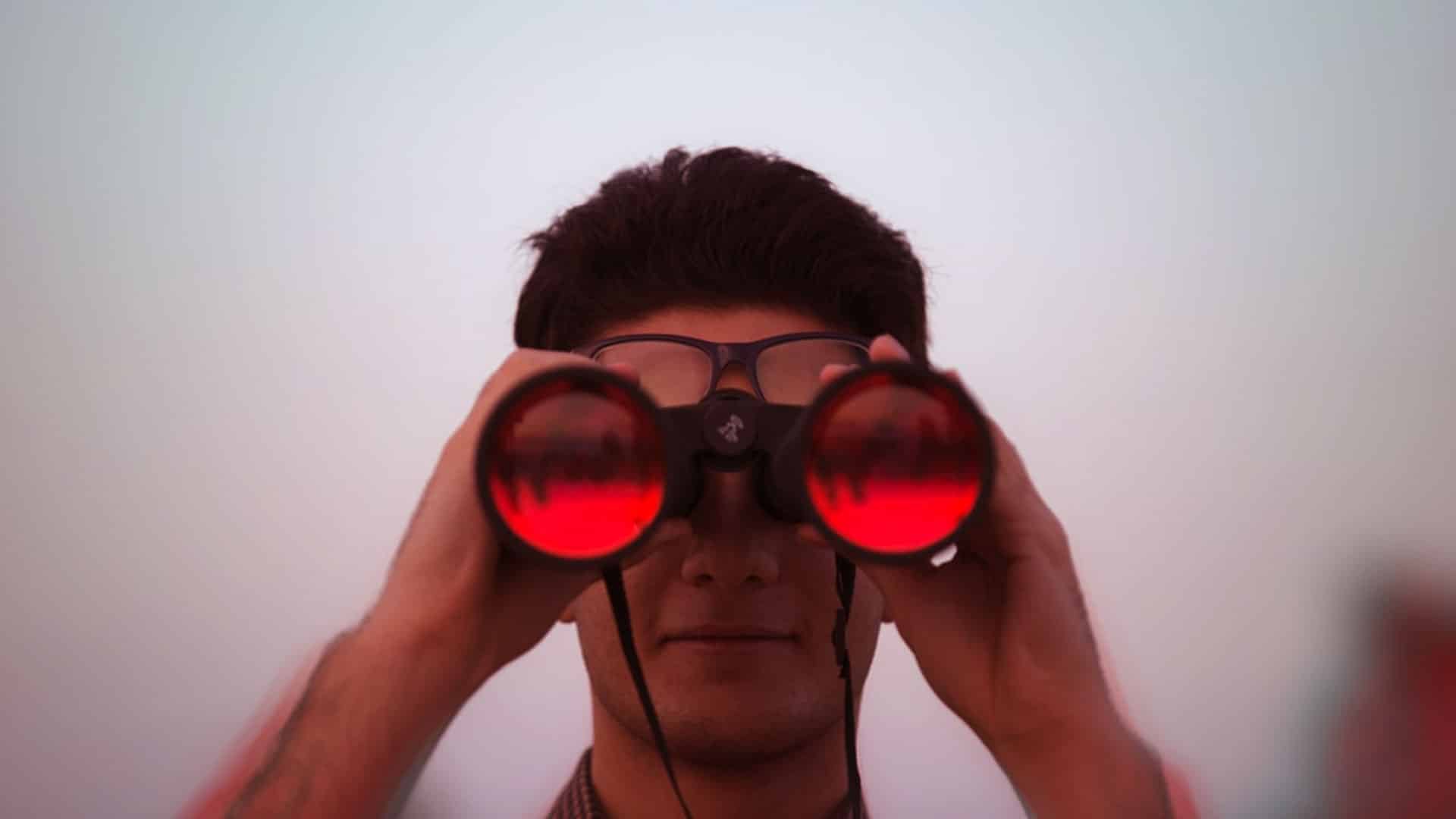 homme tenant dans ses mains des jumelles et regardant dans les jumelles de couleur rouge